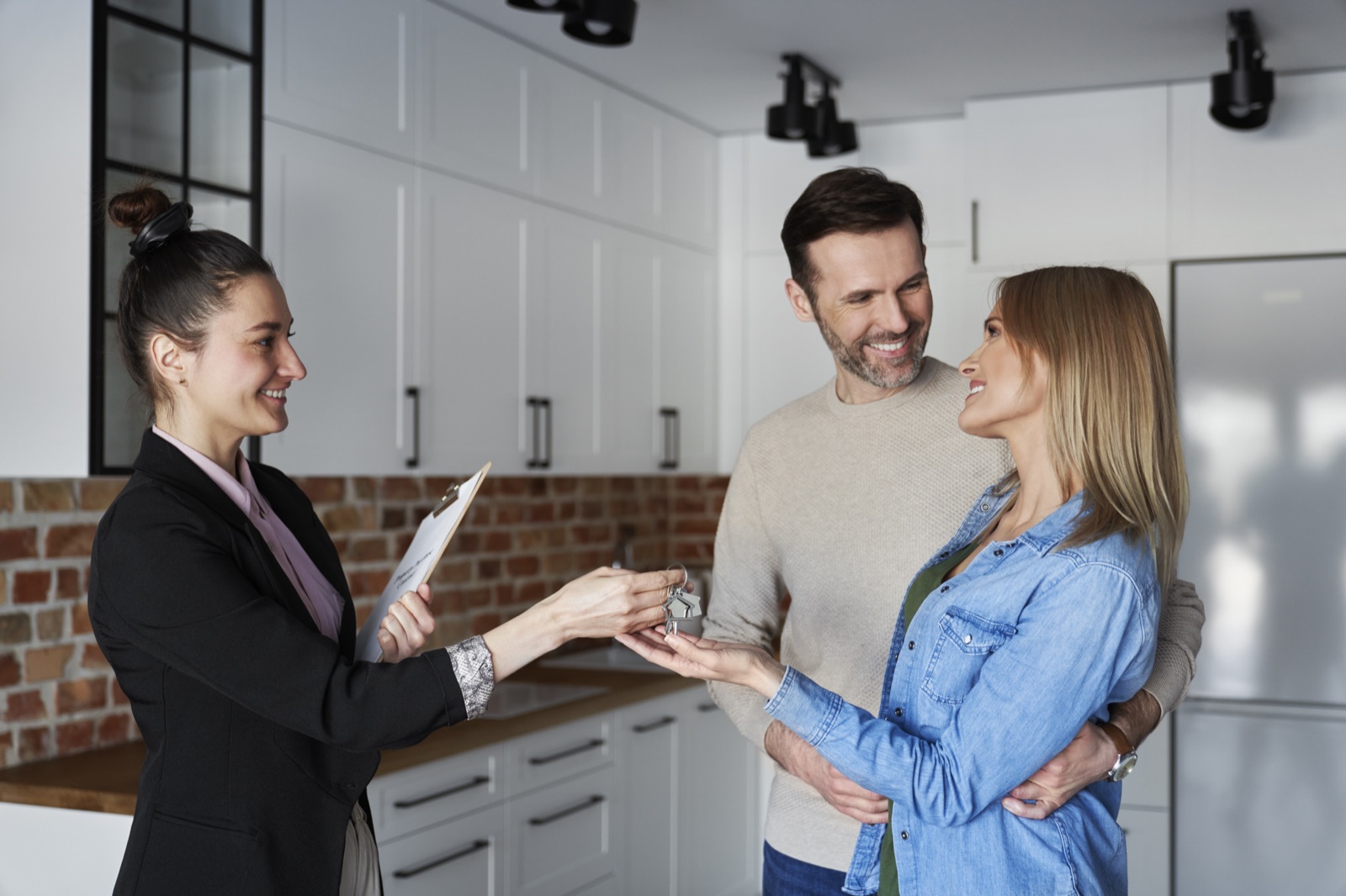 An agent handing keys to a happy couple in their new kitchen